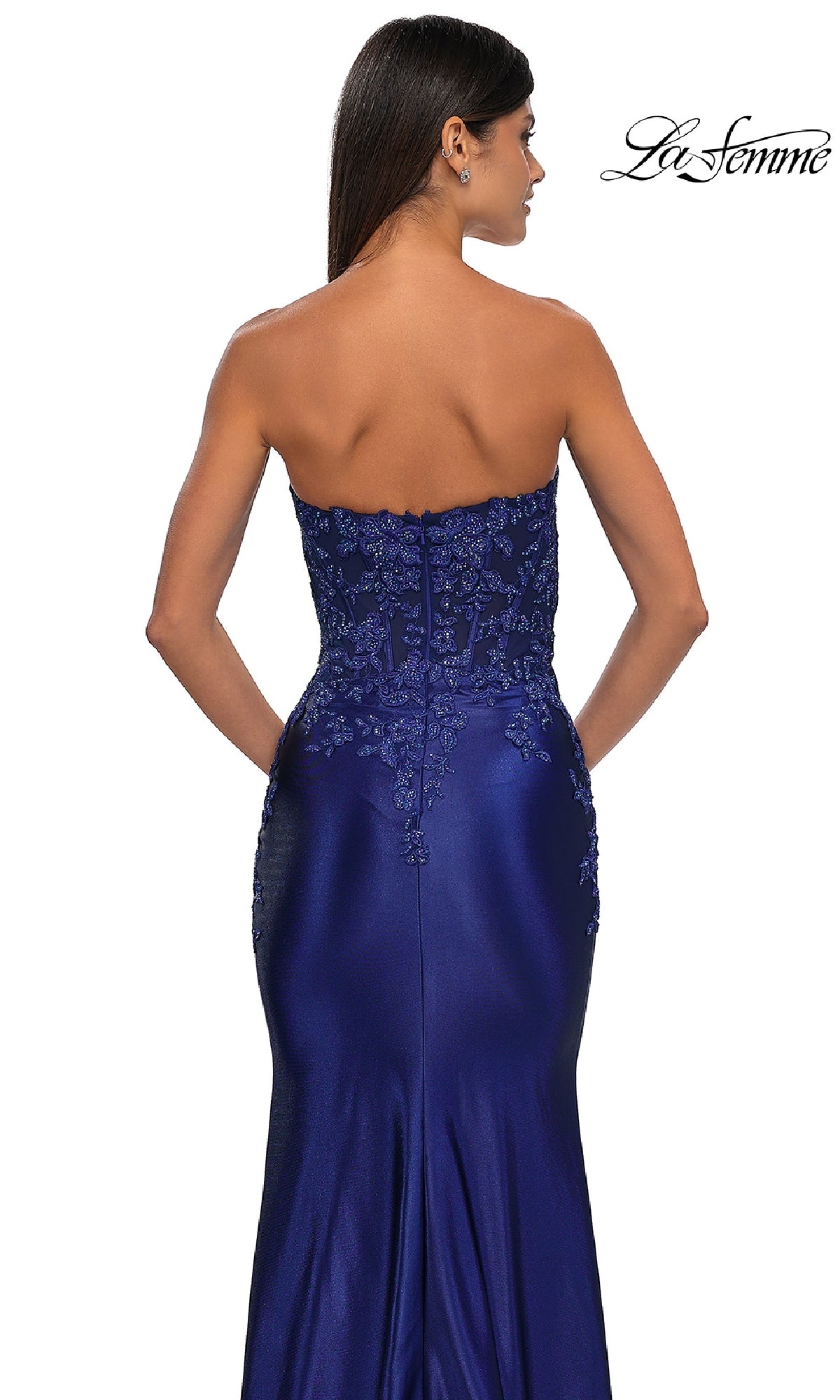 A woman models the La Femme 32582, a tight strapless long prom dress in royal blue with lace details and a beaded bodice, shown from the back against a white background.